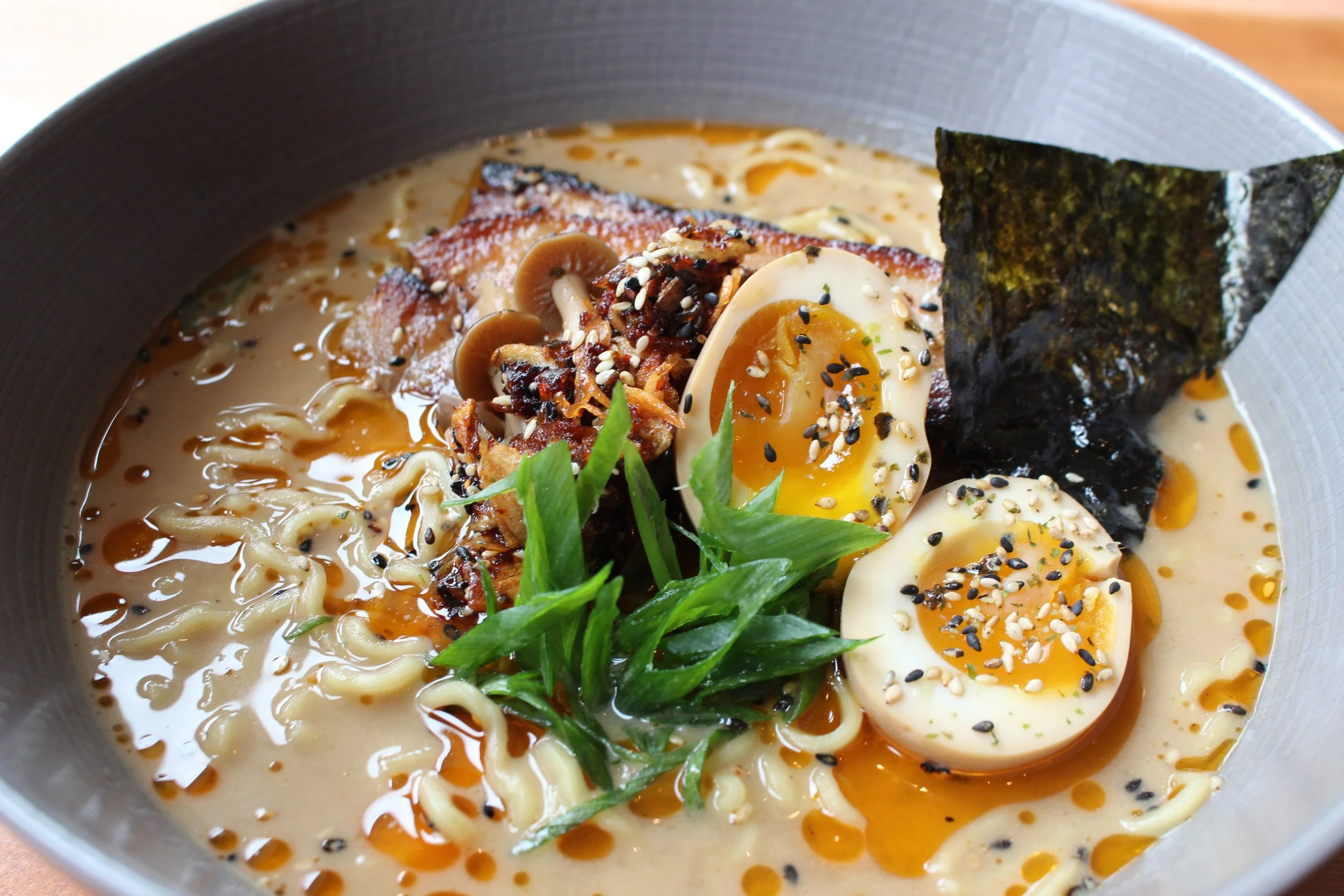 A bowl of ramen with soft-boiled eggs, seaweed, green onions, shredded meat, mushrooms, sesame seeds, and spicy broth.