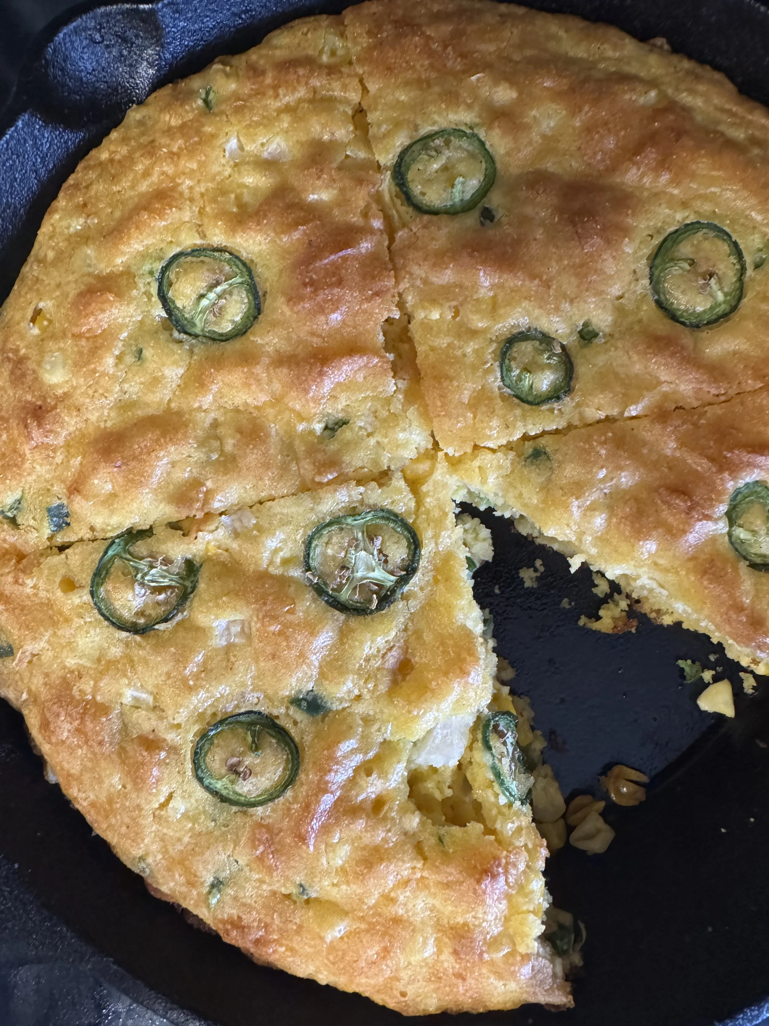 A close-up of a slice of frittata with sliced jalapeño peppers on top, cooked in a black skillet.