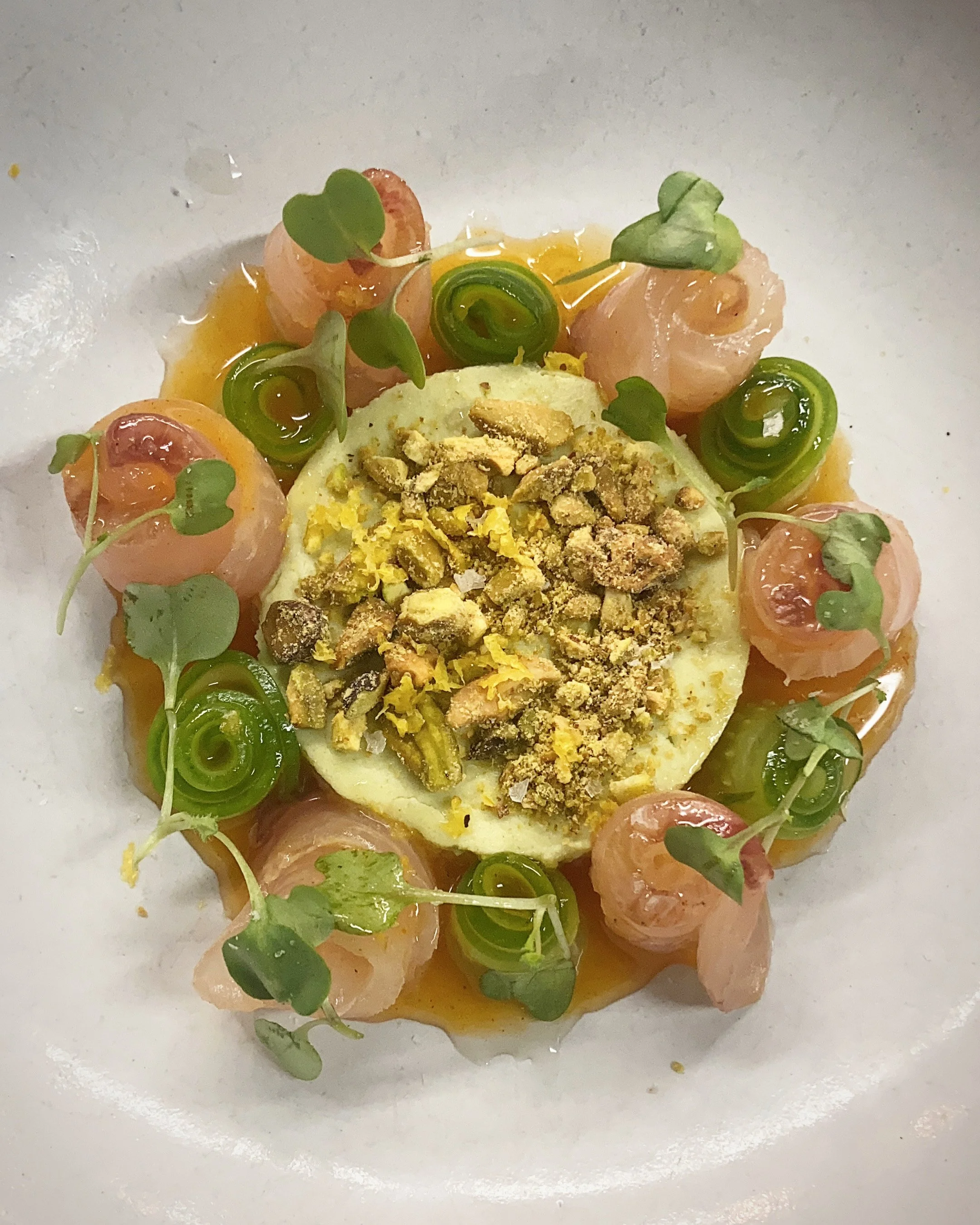 Dish with sliced radish topped with chopped nuts, garnished with microgreens, drizzled with sauce, served on a white plate.