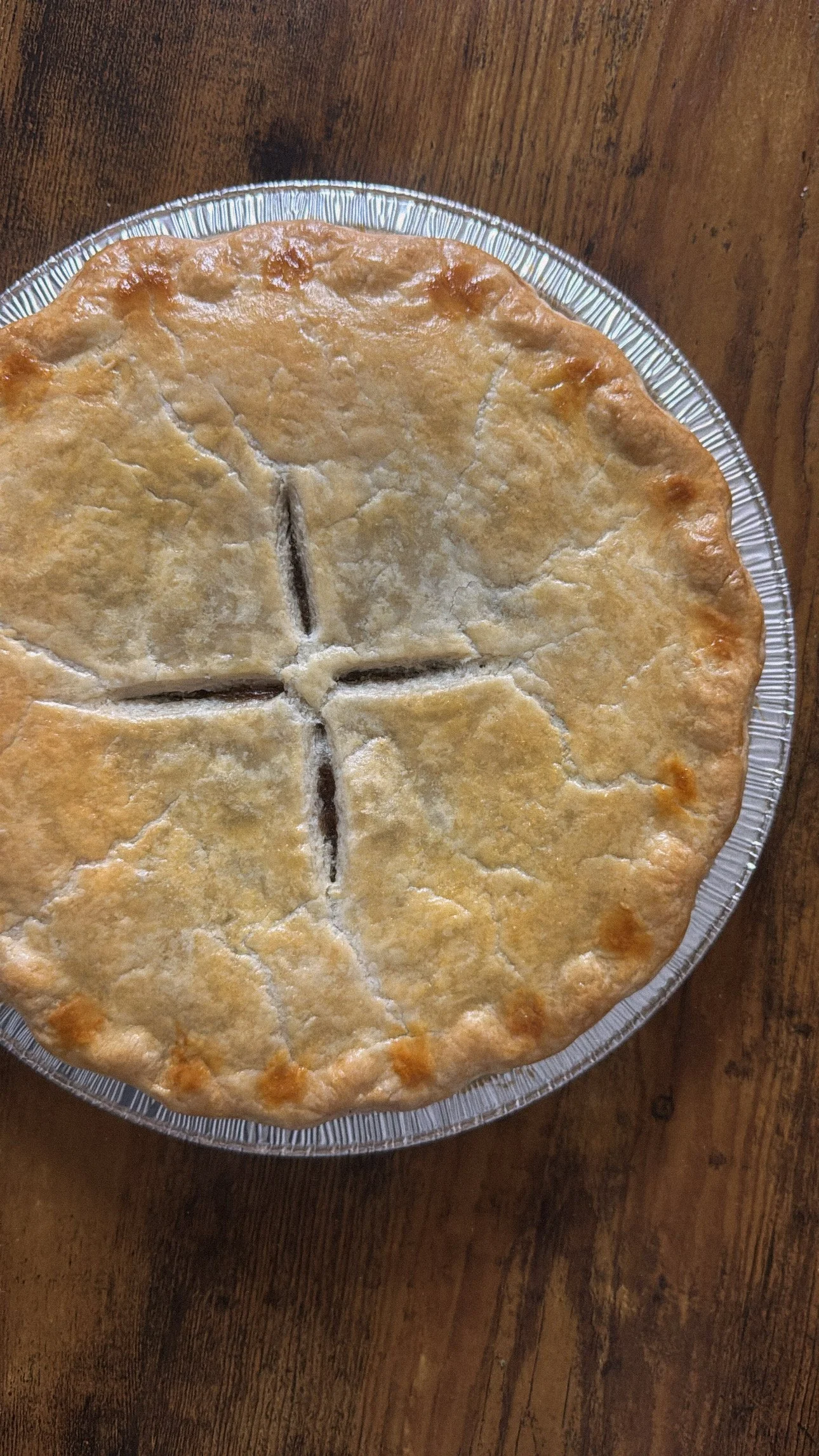 A pie with a golden crust on a clear glass plate, placed on a wooden surface.
