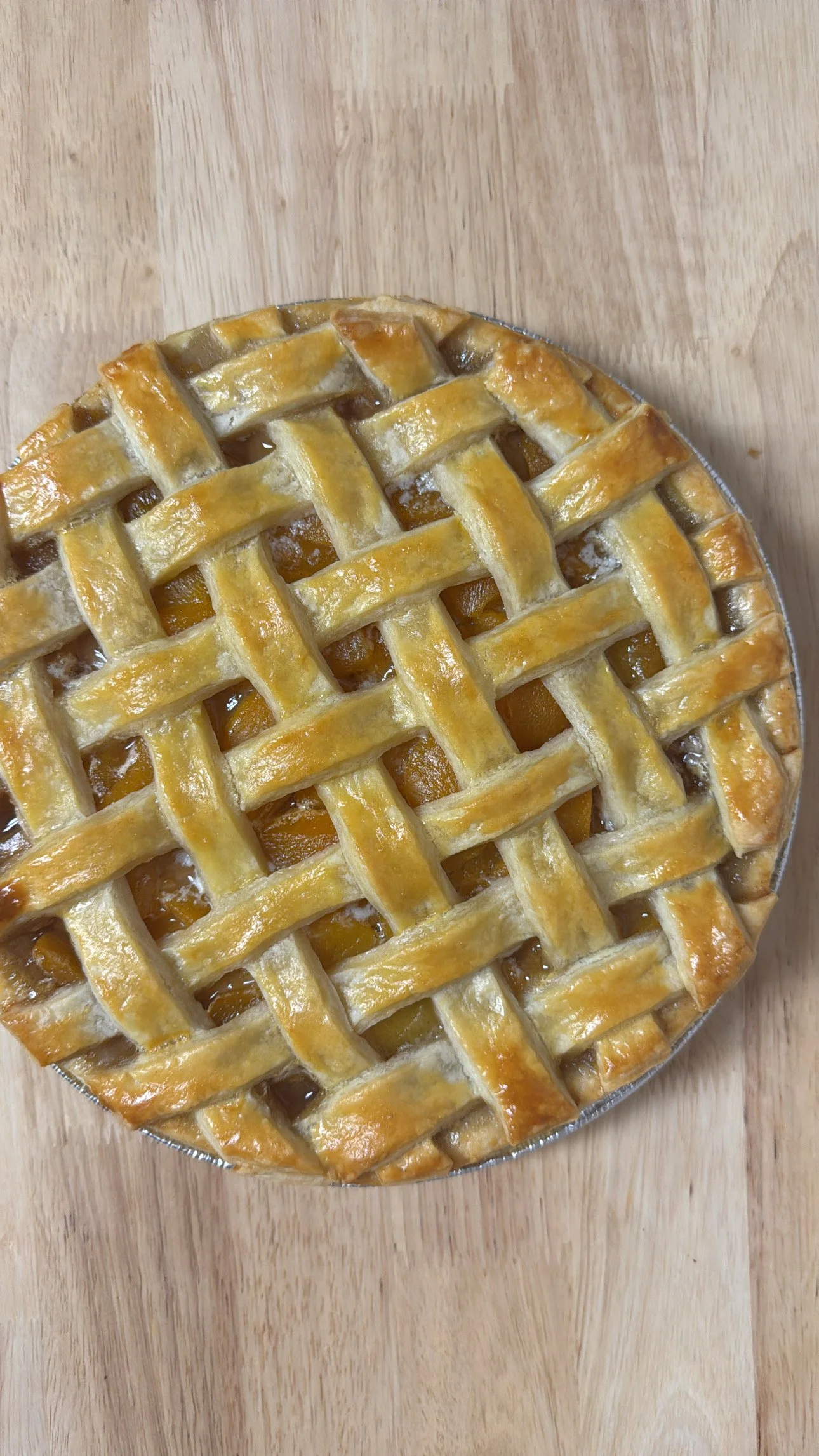 A freshly baked peach cobbler pie with a golden lattice crust on a wooden surface.