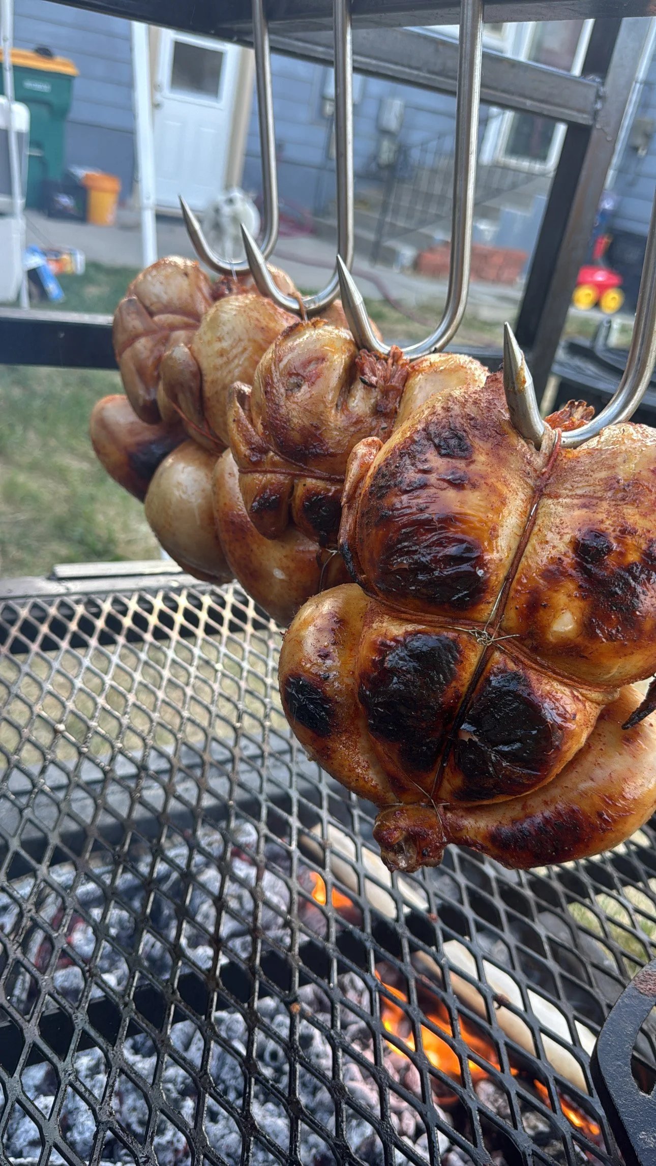 Chicken smoking on a BBQ grill over charcoal with visible flames.