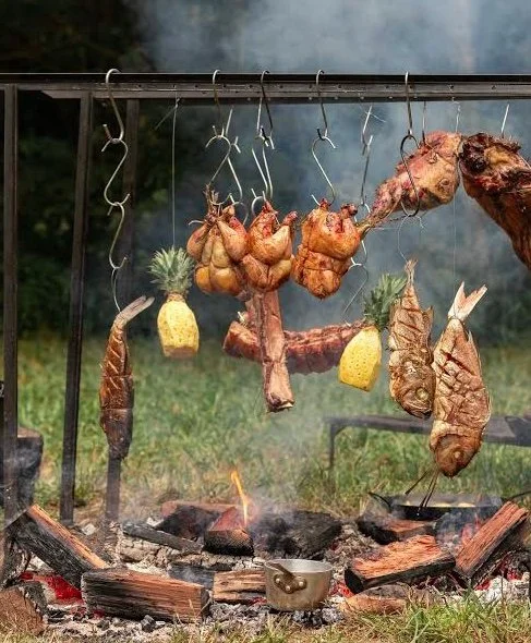Meat and pineapples roasting over an outdoor fire with smoke and flames visible.