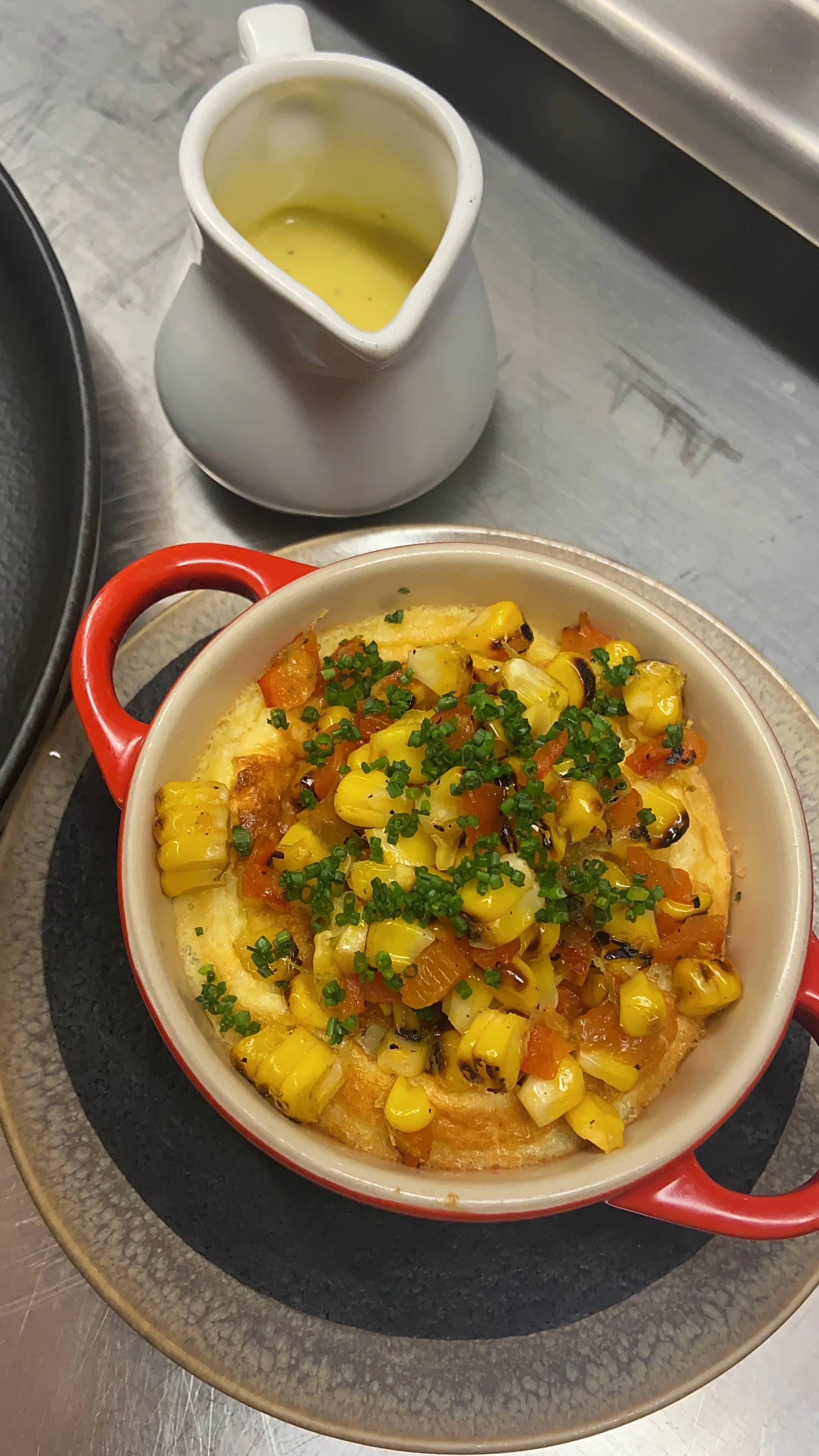 Baked dish topped with corn, chopped tomatoes, and green herbs, served in a red casserole dish.
