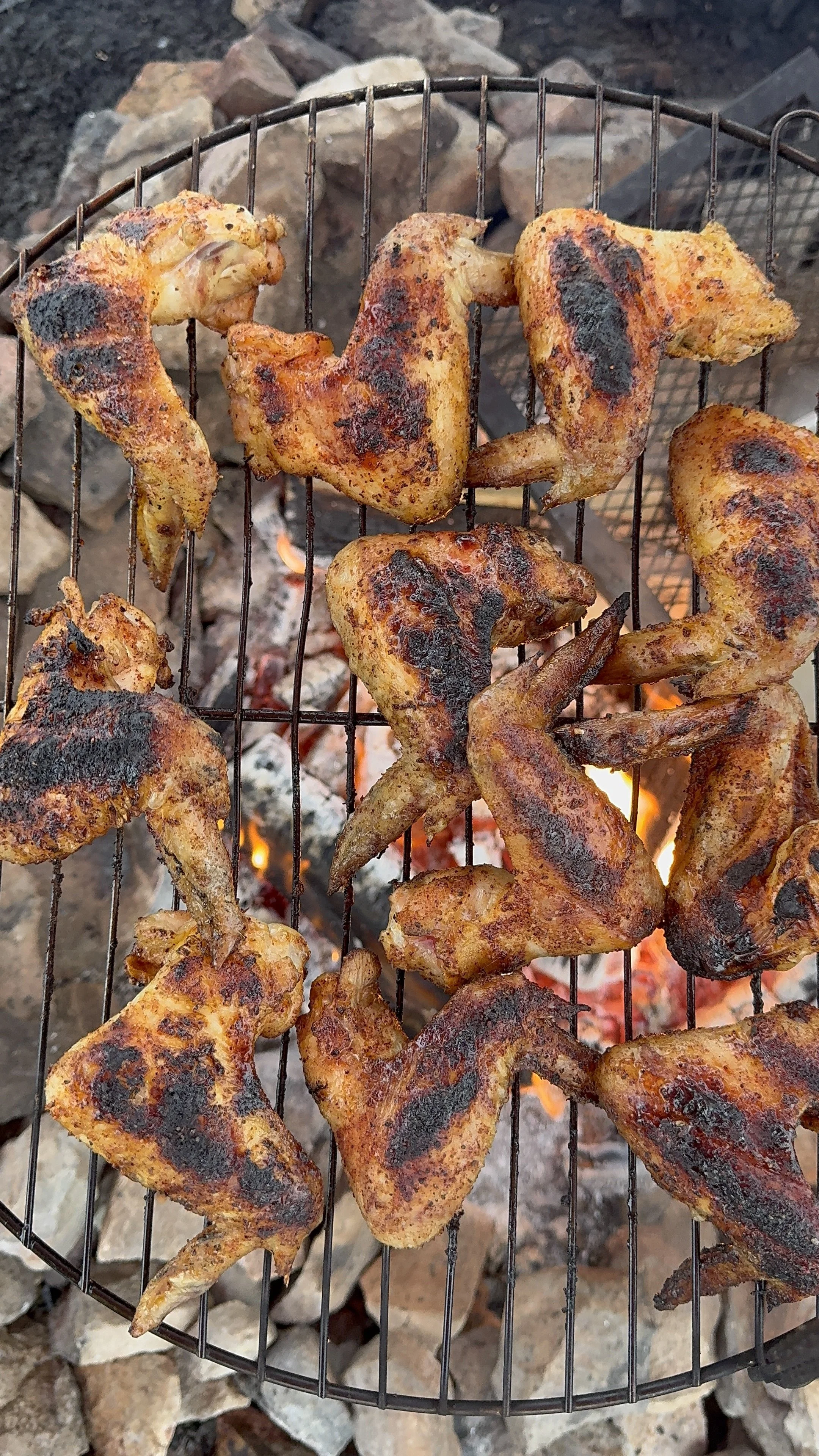 Grilled chicken pieces on a wire rack over a charcoal fire with rocks around.