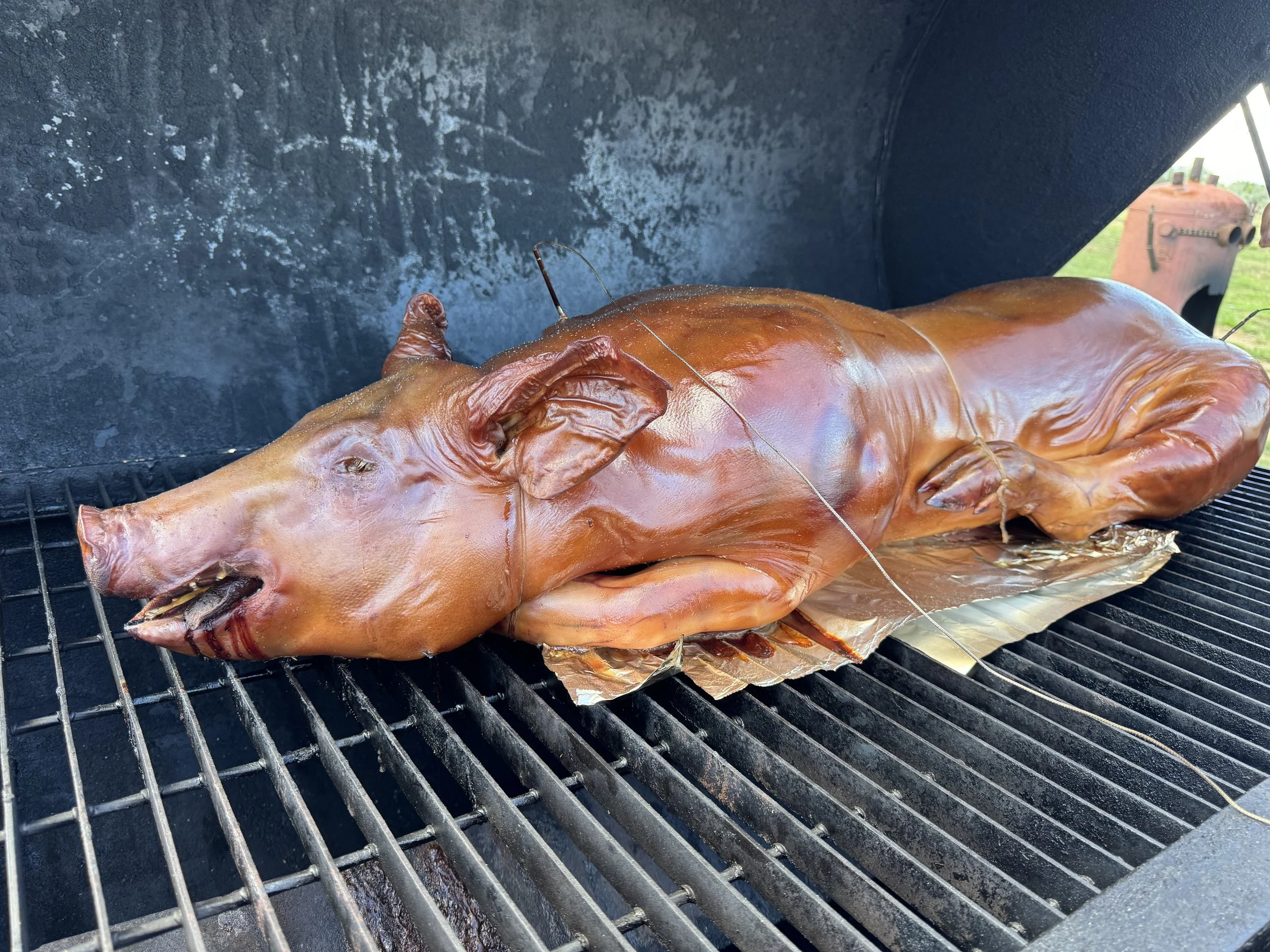 A whole pig being roasted on a grill, with the pig's skin appearing crisp and golden, and some equipment visible in the background.