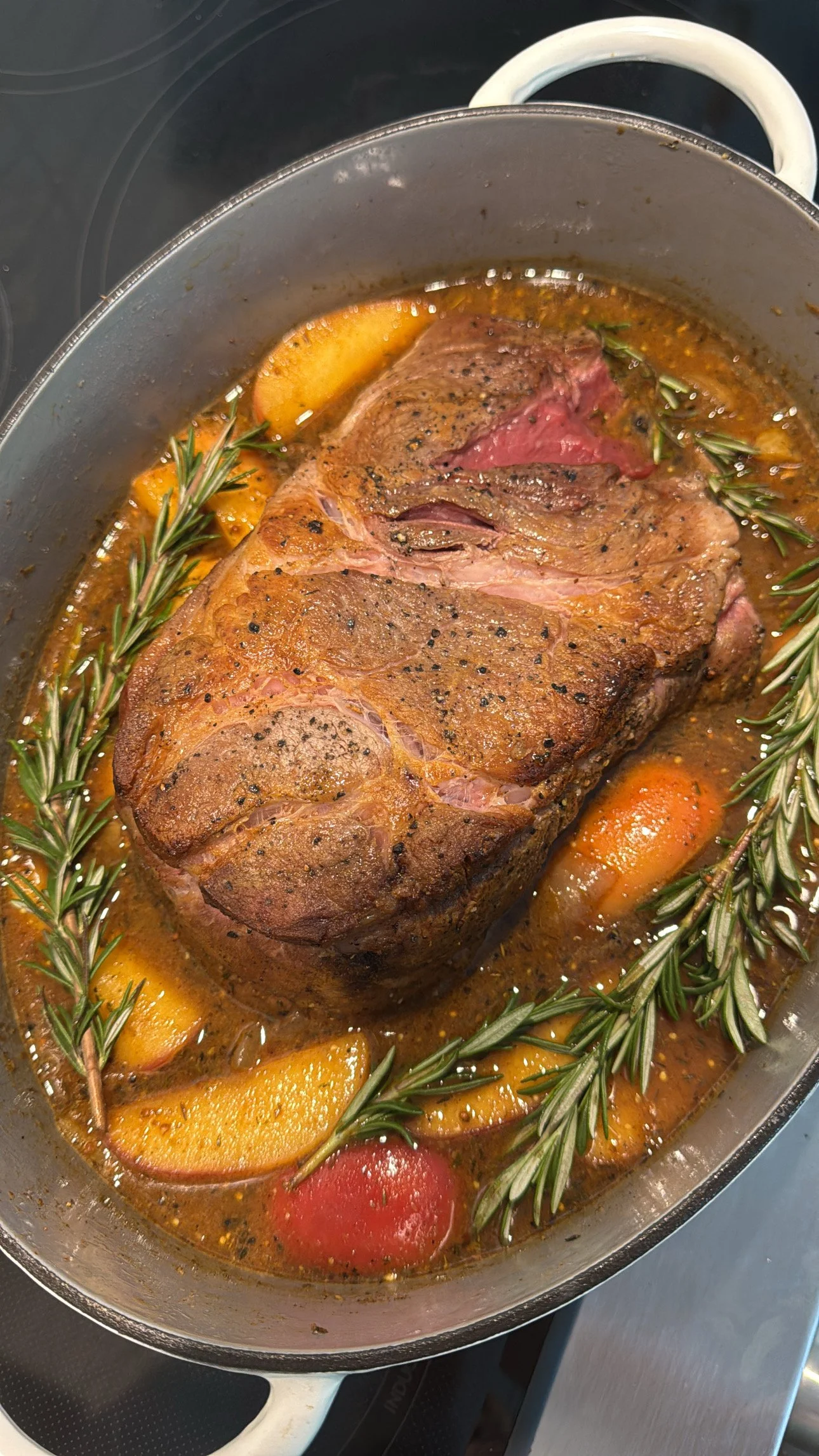 A cooked roast beef with herbs and vegetables in a pan.