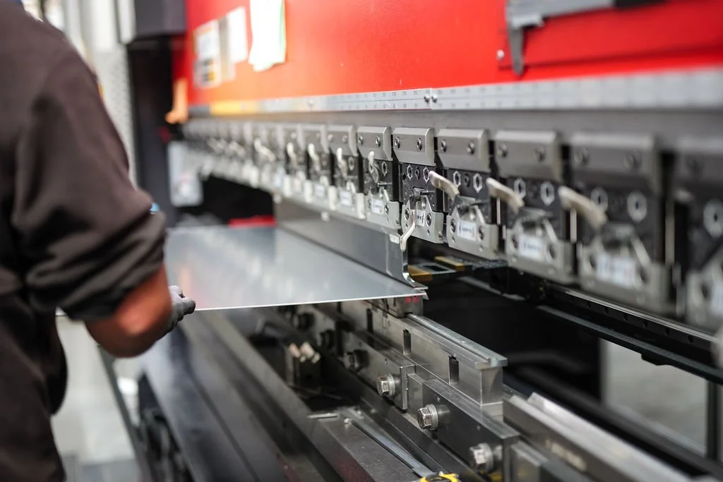 A worker operating a large industrial sheet metal punch press machine in a manufacturing setting.