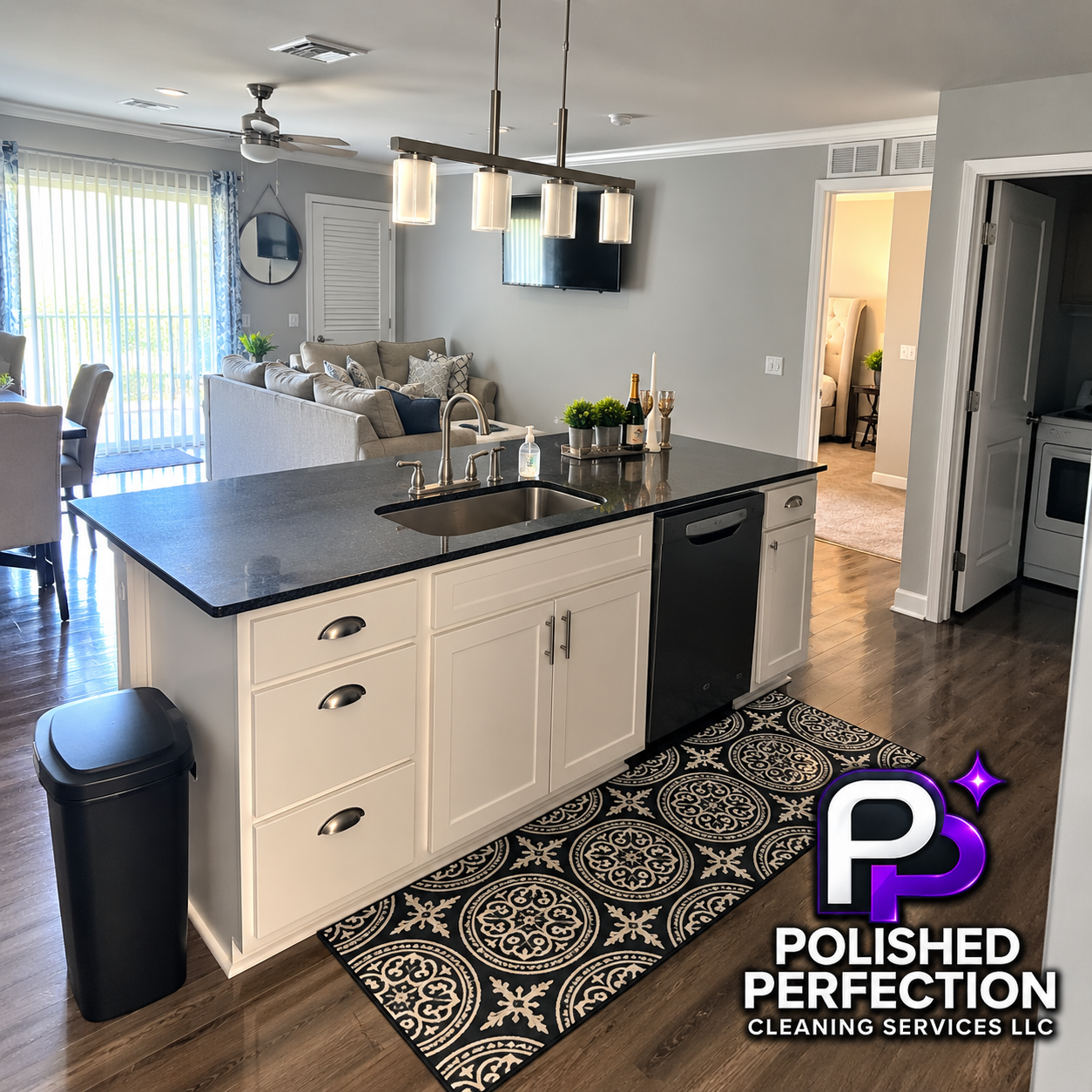 Clean modern kitchen with white cabinets, black countertop, sink, and stainless steel faucet. Decorated with champagne, candles, and plants. Open living area with gray walls, TV, and dining table near sliding glass door. Polished Perfection Cleaning Services LLC logo in the bottom right corner.