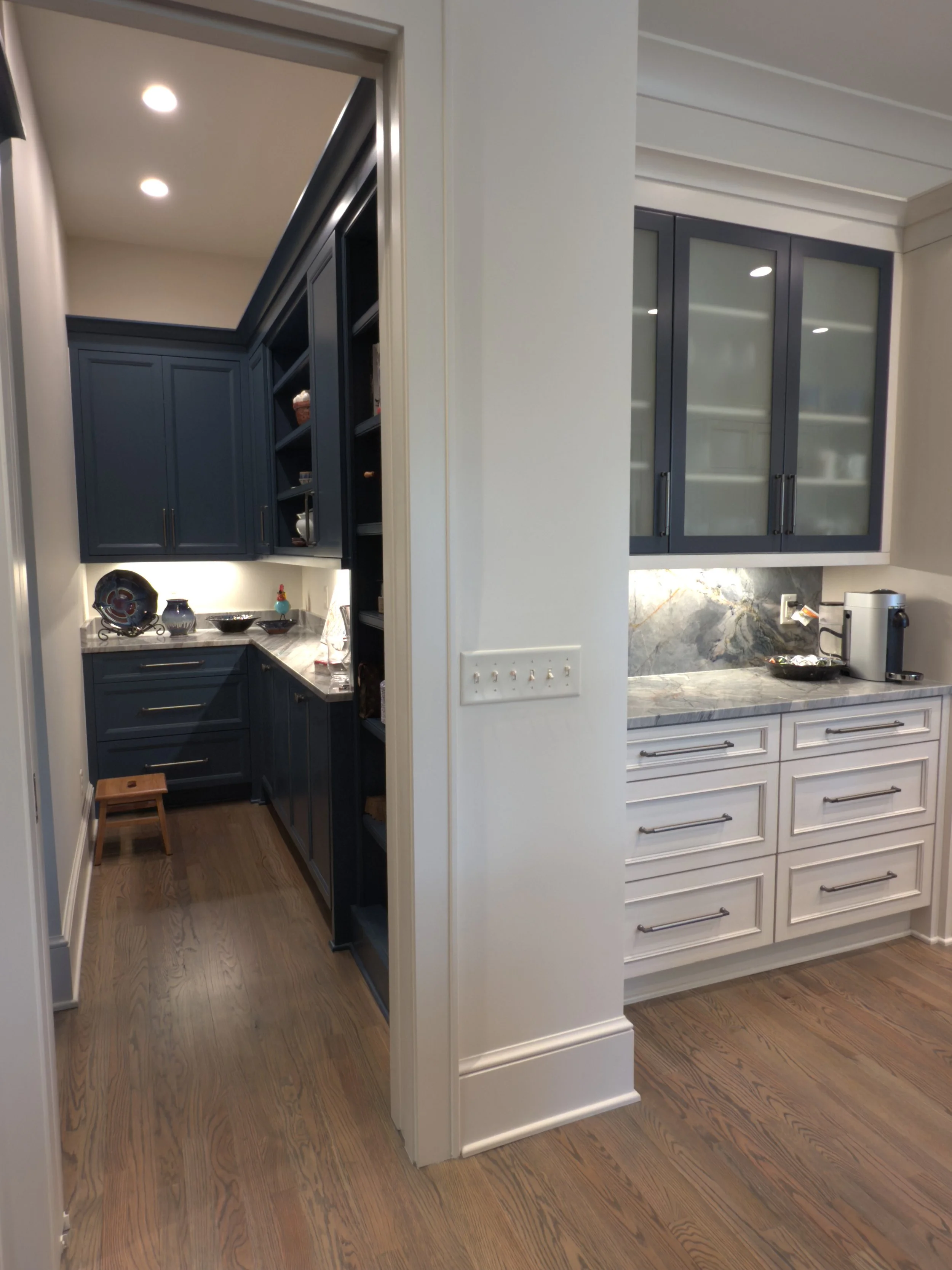 Kitchen with dark blue and white cabinets, wood flooring, and kitchen appliances including a coffee maker.