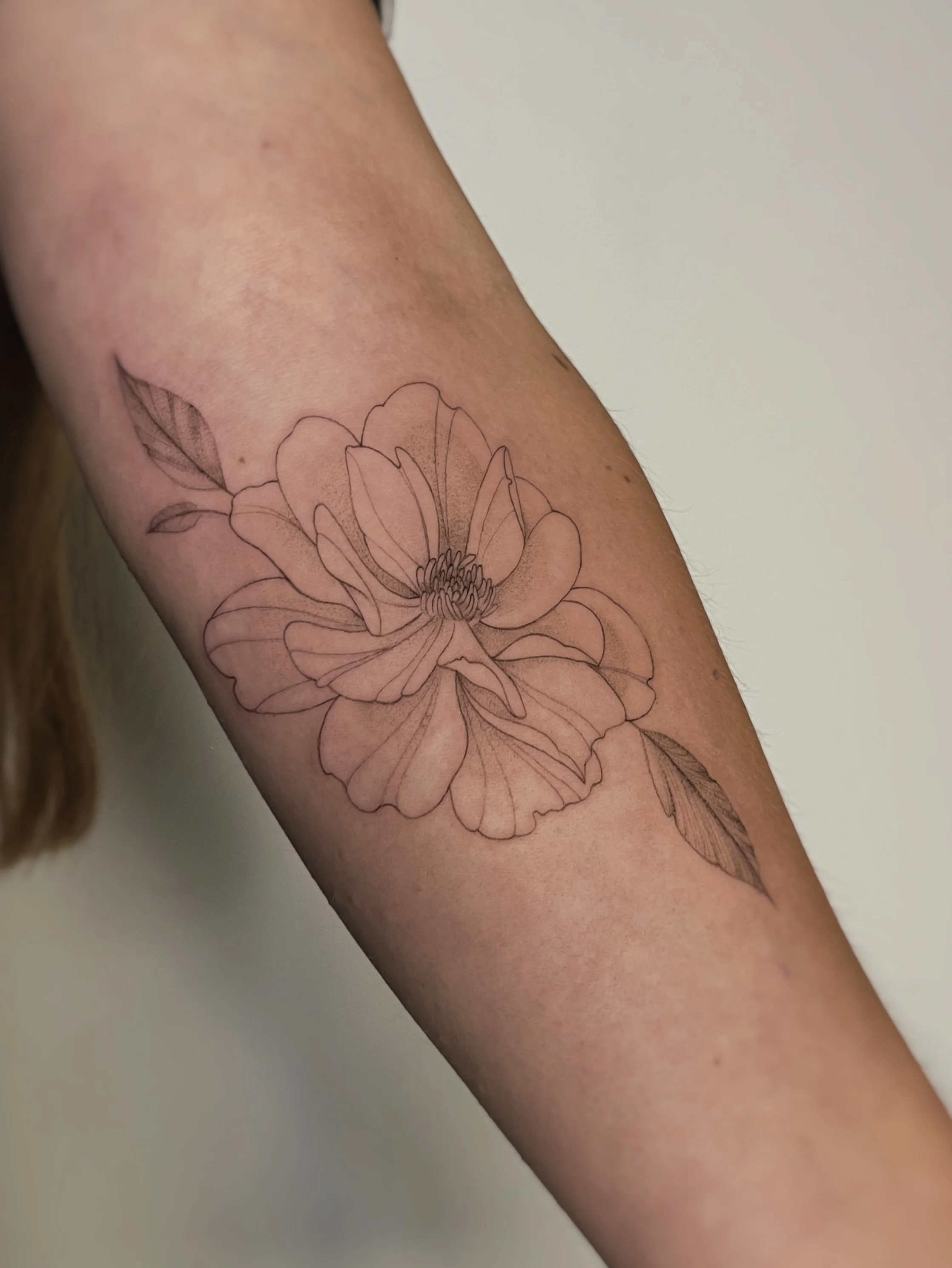 A delicate wild peony tattoo on the inner forearm.