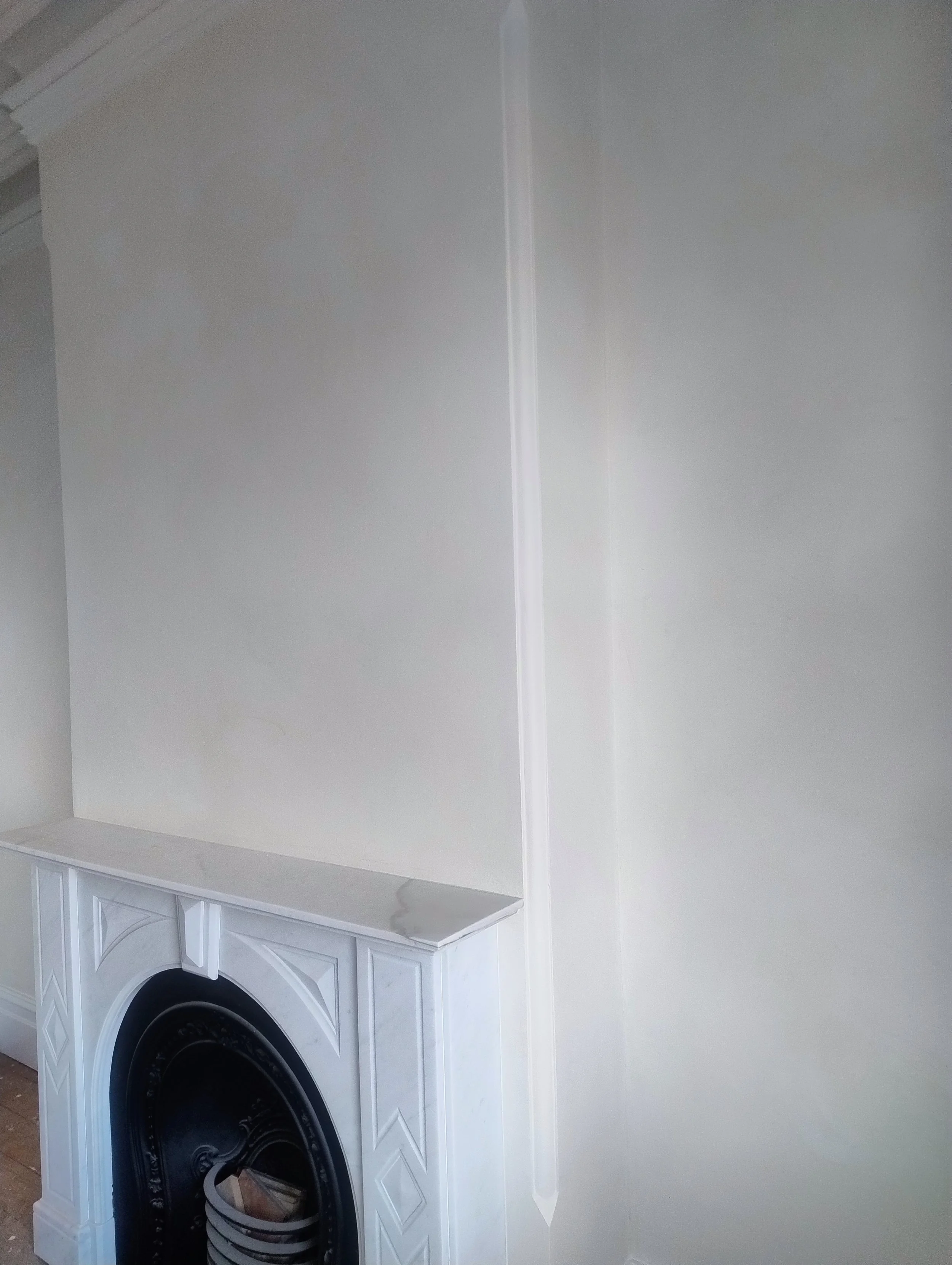 The image shows a grasello venetian plaster wall with a built-in fireplace with a decorative mantel and black interior. The wall has a corner with minimal crown molding at the top.