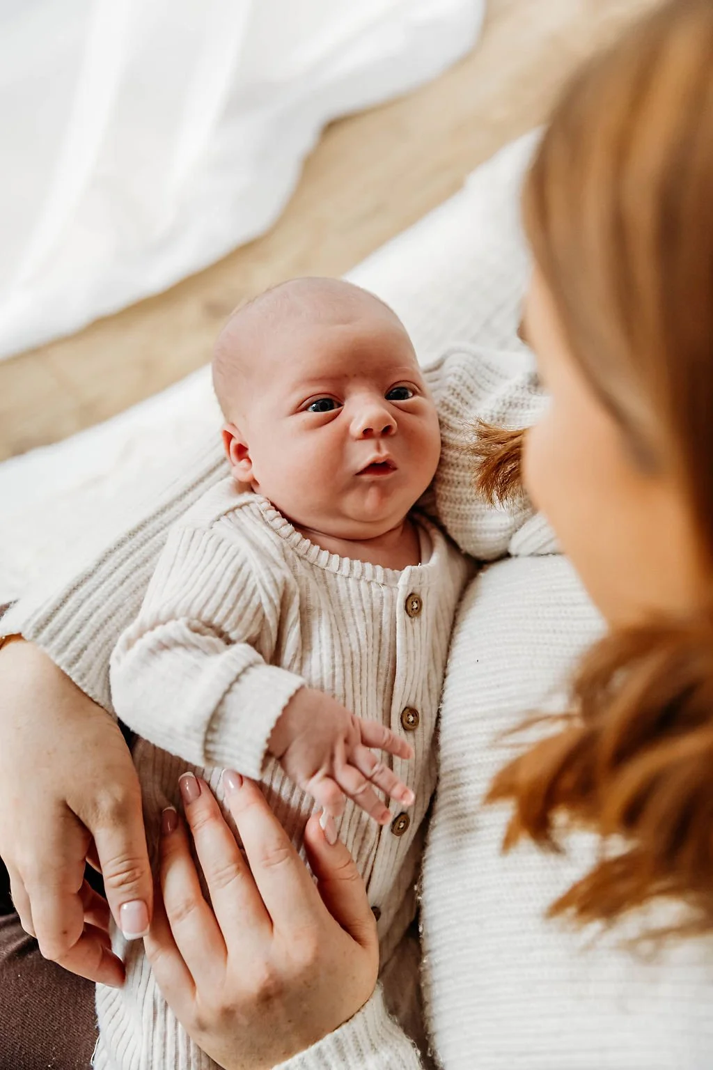 A baby with big blue eyes lying on a woman's chest, looking up at her, while she gently holds the baby on her chest.