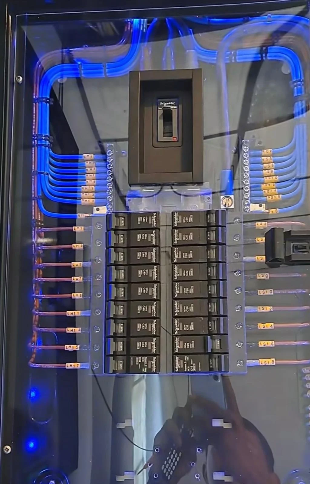 An electrical panel with circuit breakers, wiring, and a main switch, illuminated by blue LED lights.