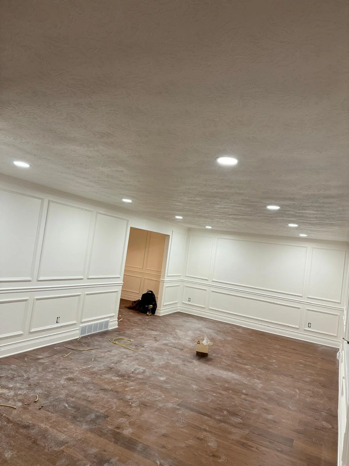 Empty room with white walls, white paneling, and hardwood floors under construction, with scattered tools and supplies.