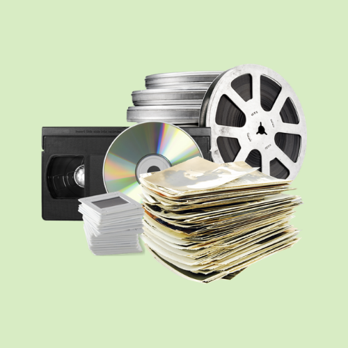 Stack of VHS tapes, film reels, photo slides, CDs, and a pile of printed photos ready for digitization.