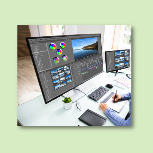 A person editing photos on a large computer monitor with color wheels and a landscape image, using a graphics tablet and smaller monitors for viewing thumbnails.