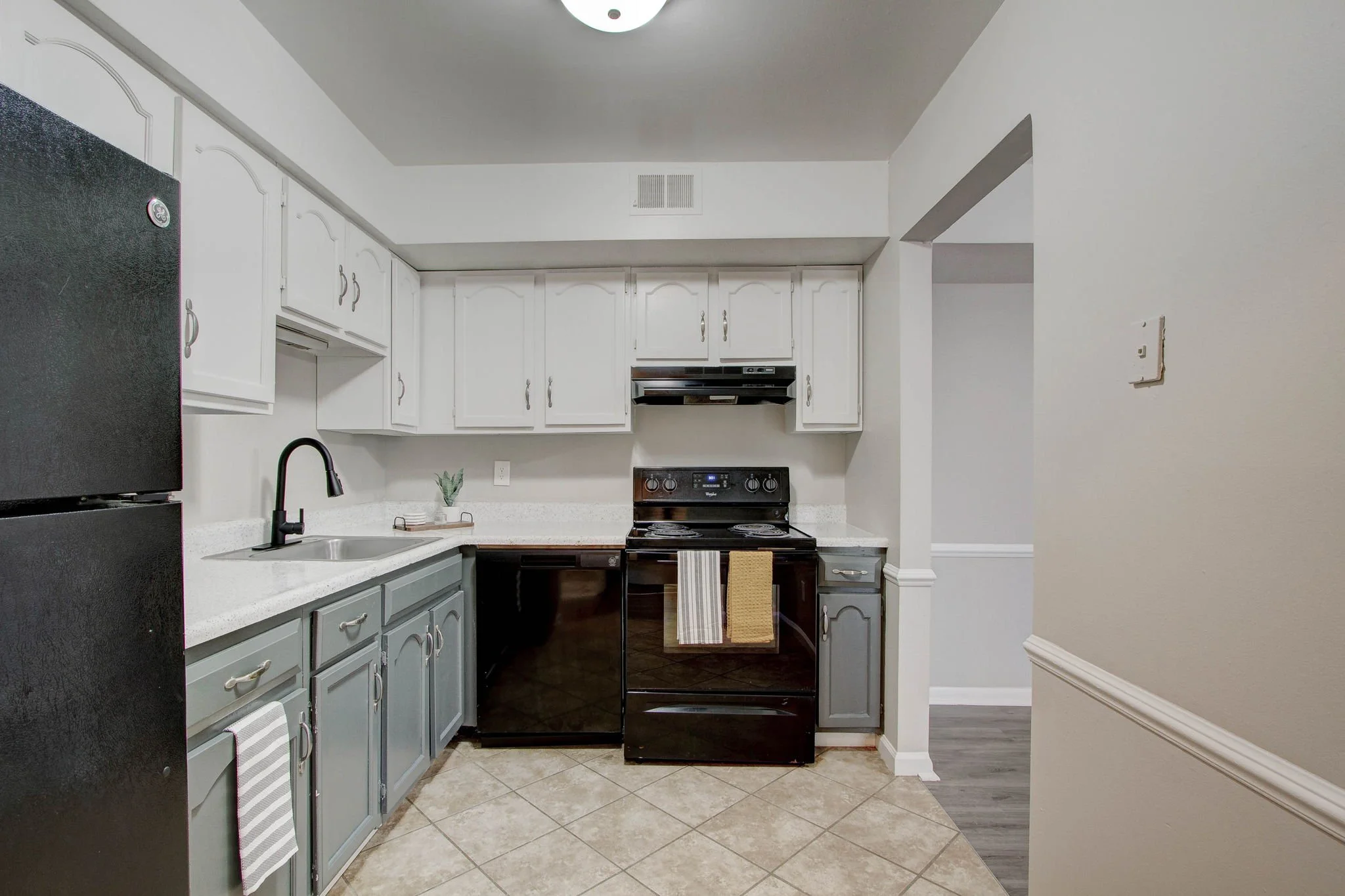 Kitchen with black refrigerator, white upper cabinets, gray lower cabinets, black stove, and black dishwasher. Towel hanging on oven handle, small plant on countertop.