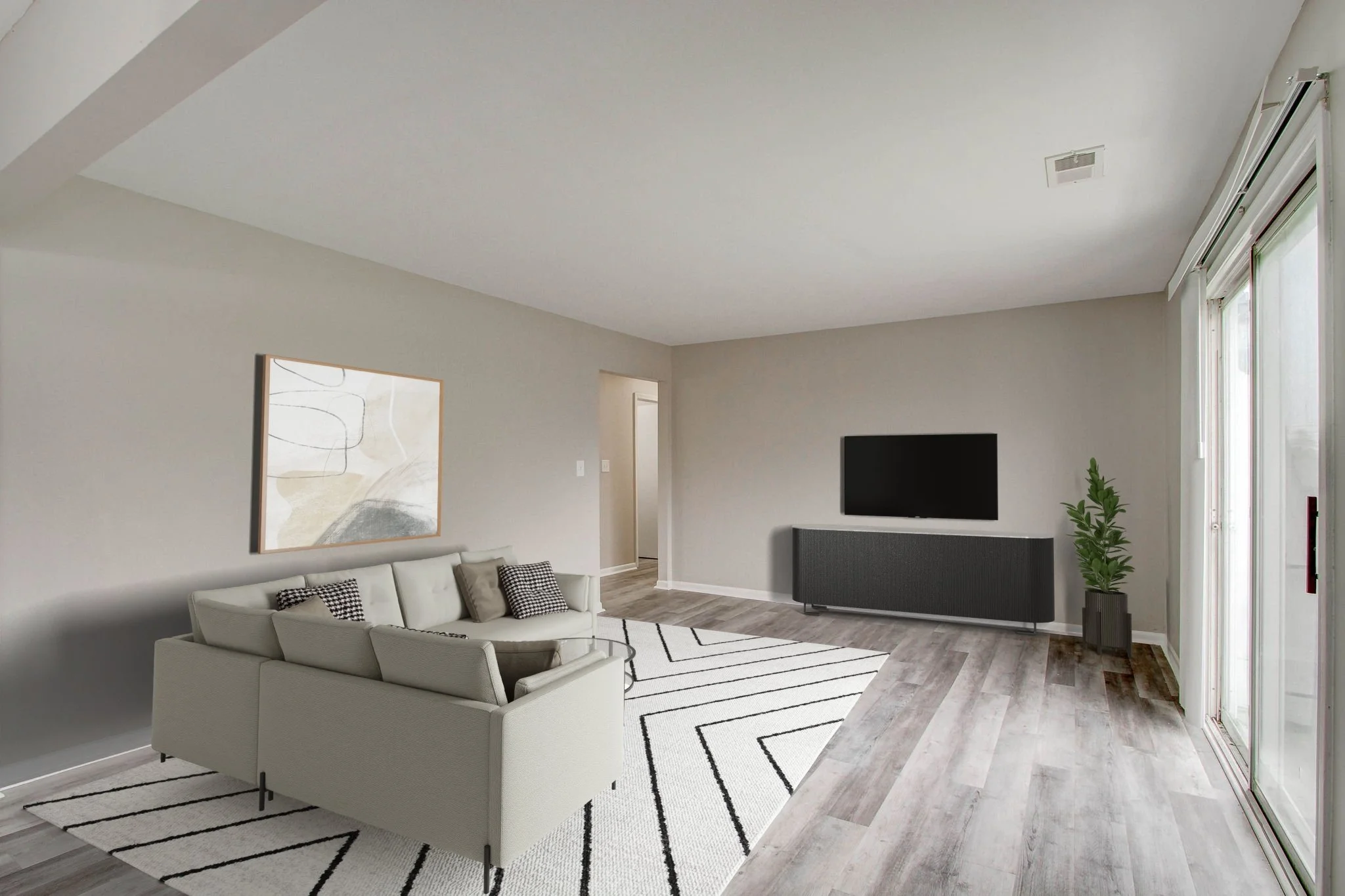 Modern living room with a gray couch, black and white patterned pillows, abstract artwork on the wall, a black TV mounted on the wall, a gray media console, a green potted plant, a black and white geometric rug, and sliding glass doors to the right.