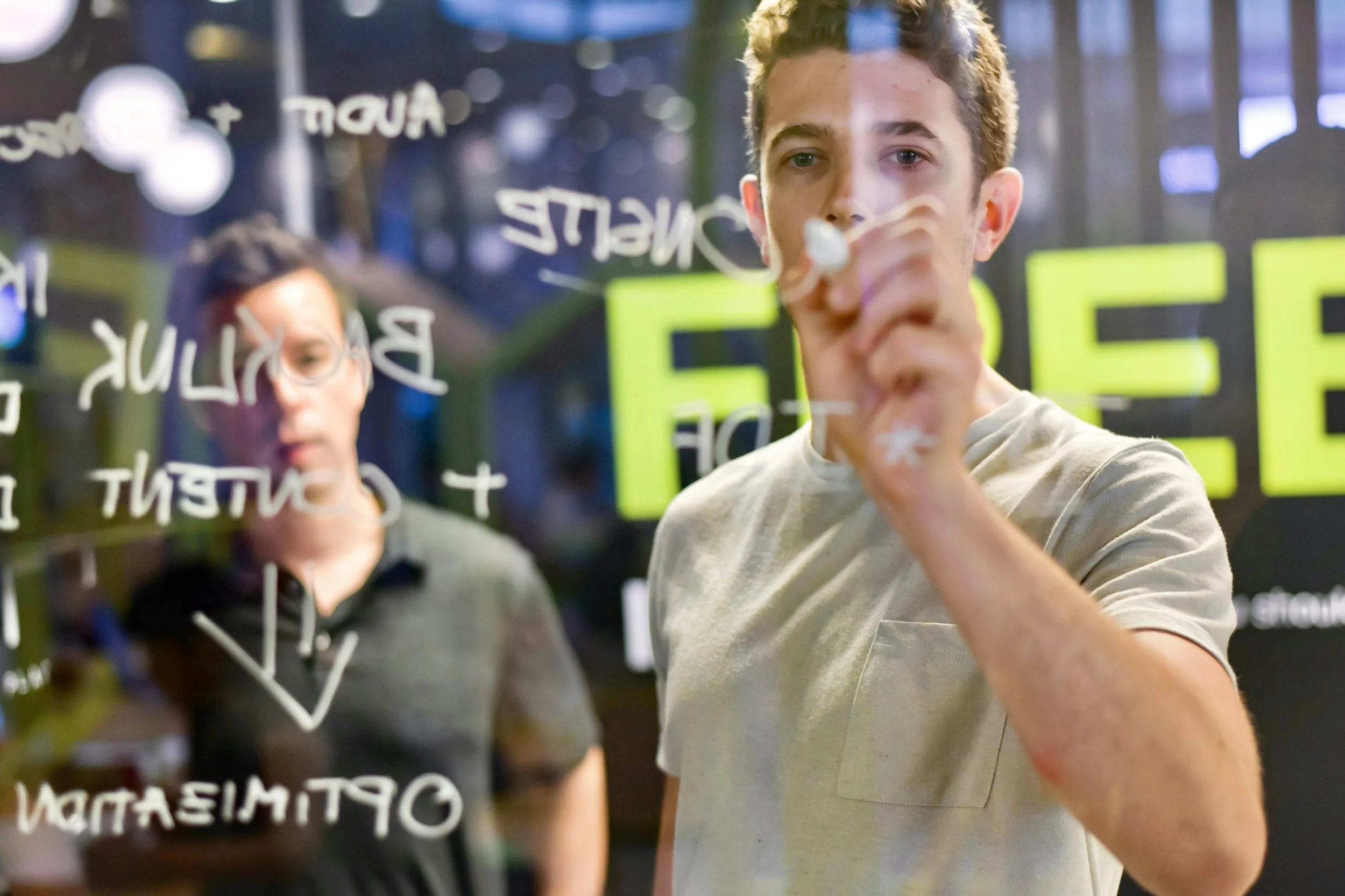 Two young men writing on a transparent board with markers, with text about education and inspiration visible in the background.