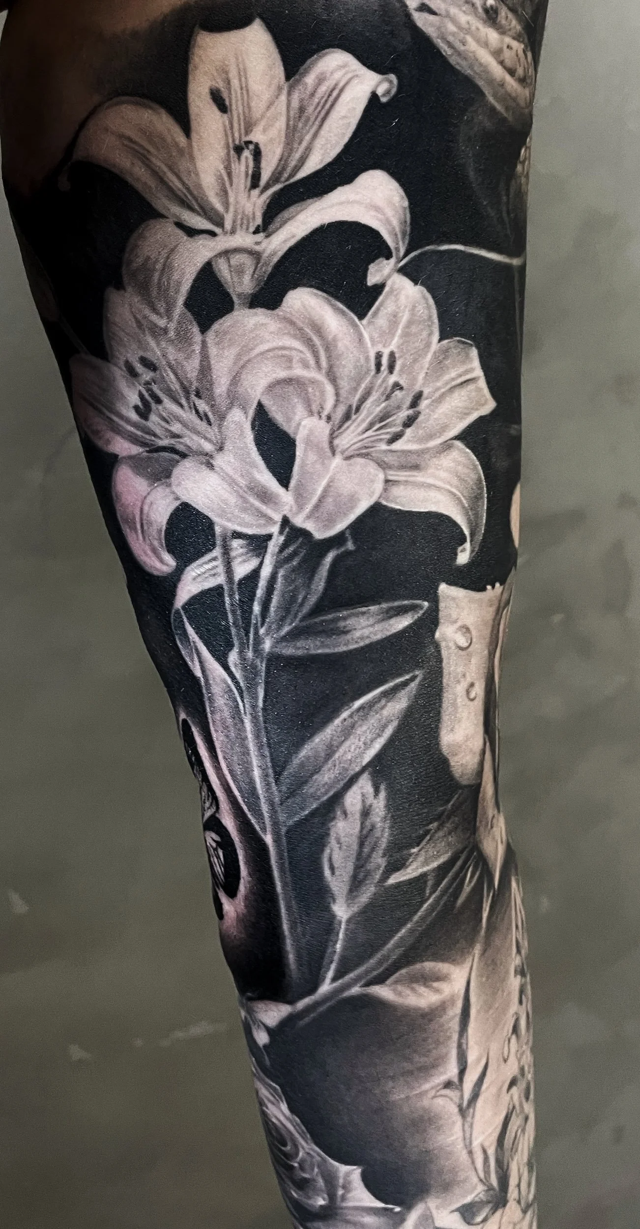 Close-up of a black and white floral tattoo featuring lilies on a person's leg.