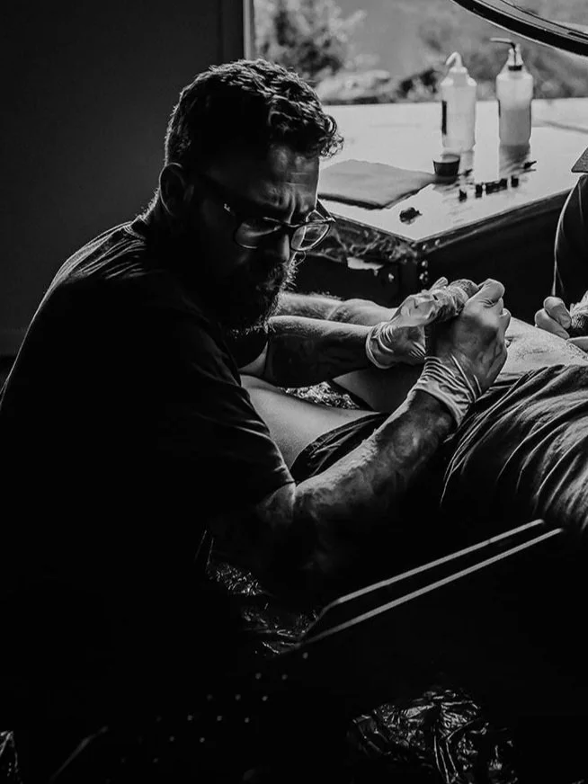 A tattoo artist working on a client in a tattoo studio, with tattoo supplies on the table nearby.
