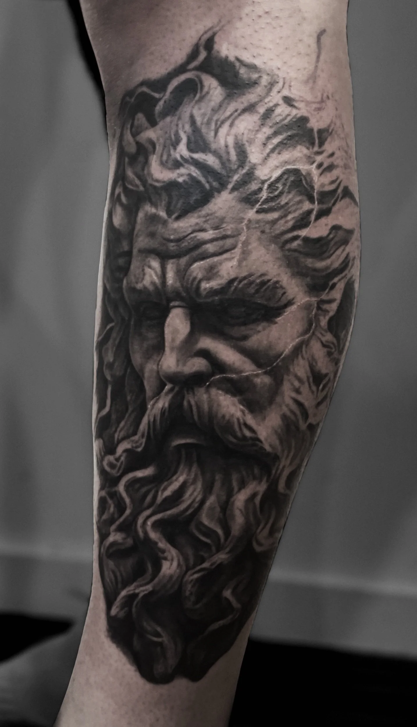 Black and gray tattoo of a classical Roman or Greek sculpture of a bearded man's face with intricate details.
