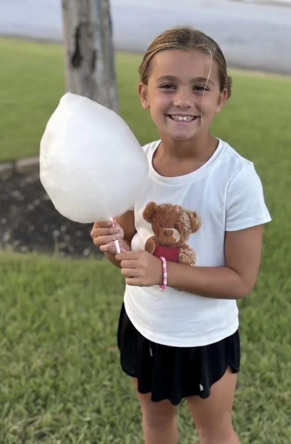 Smiling young girl holding a large piece of cotton candy outdoors.