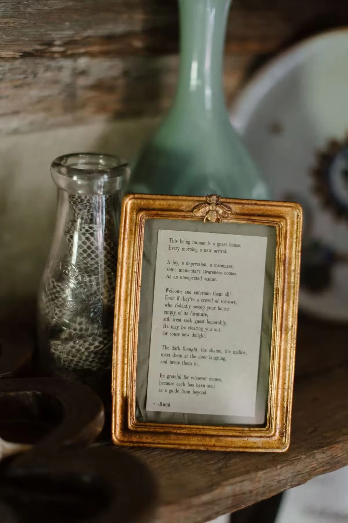 A framed poem on a wooden surface next to a clear vase and a green bottle.