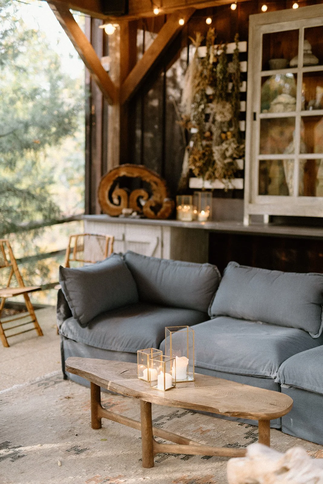 Cozy rustic living room with gray sofa, wooden coffee table with candles, and decor including candles, dried flowers, and wood accents.