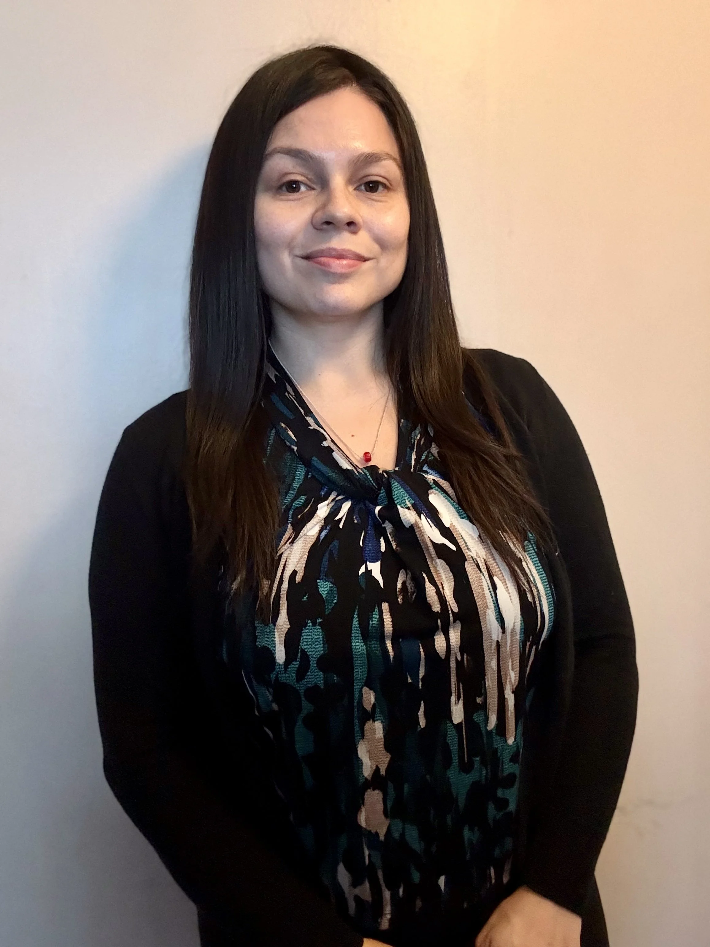 A woman in a white dress with lace details and a plunging neckline, wearing hoop earrings, lying on a mossy rock surrounded by greenery, with a bouquet of white roses and baby's breath flowers resting on the rock next to her.