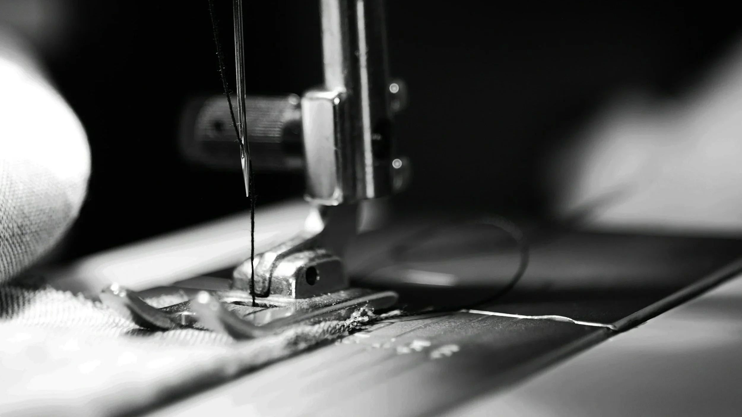 Close-up of a sewing machine needle and presser foot sewing fabric in black and white.