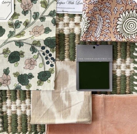 A collection of fabric samples in various patterns and colors, including floral, geometric, and plain, displayed on a woven rug with a green swatch card labeled 'The Urban Electric' placed in the center.