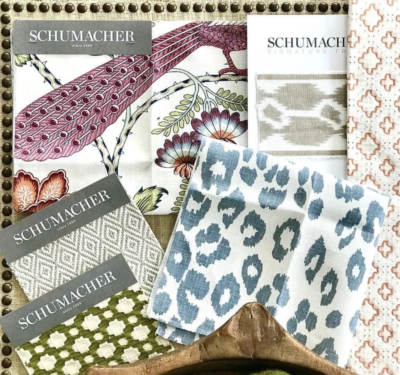 A collection of fabric swatches with various patterns and colors, including floral, animal print, geometric, and geometric designs. Some swatches have labels with the brand name "Schumacher."