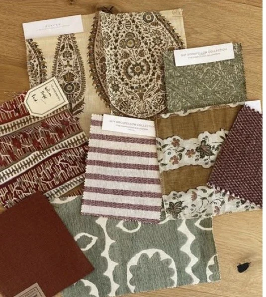 A collection of fabric swatches with various patterns and colors, including floral, geometric, and striped designs, lying on a wooden surface.