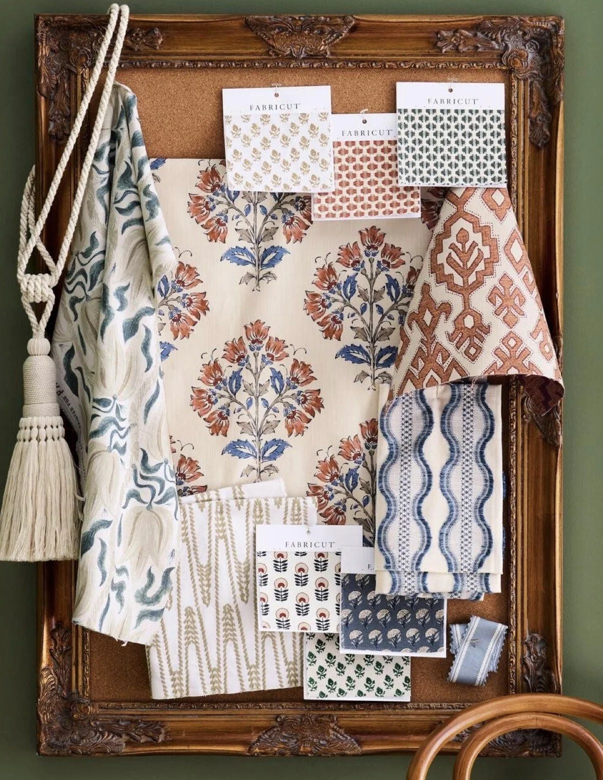 Display of fabric swatches with floral and geometric patterns on a decorative wooden framing with a corkboard background.
