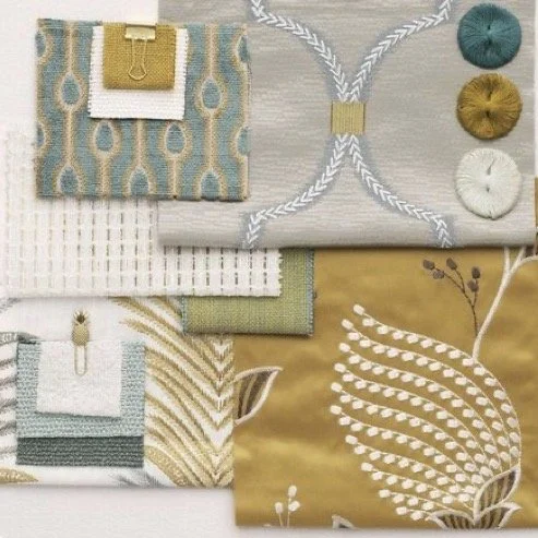 Flat lay of various fabric swatches, including patterns and textures in shades of beige, green, gray, and yellow, with sewing tools and threads.