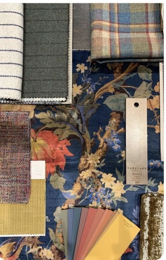 Fabric swatches and samples displayed on a decorative floral tablecloth, including striped, plaid, textured, and color sample cards.