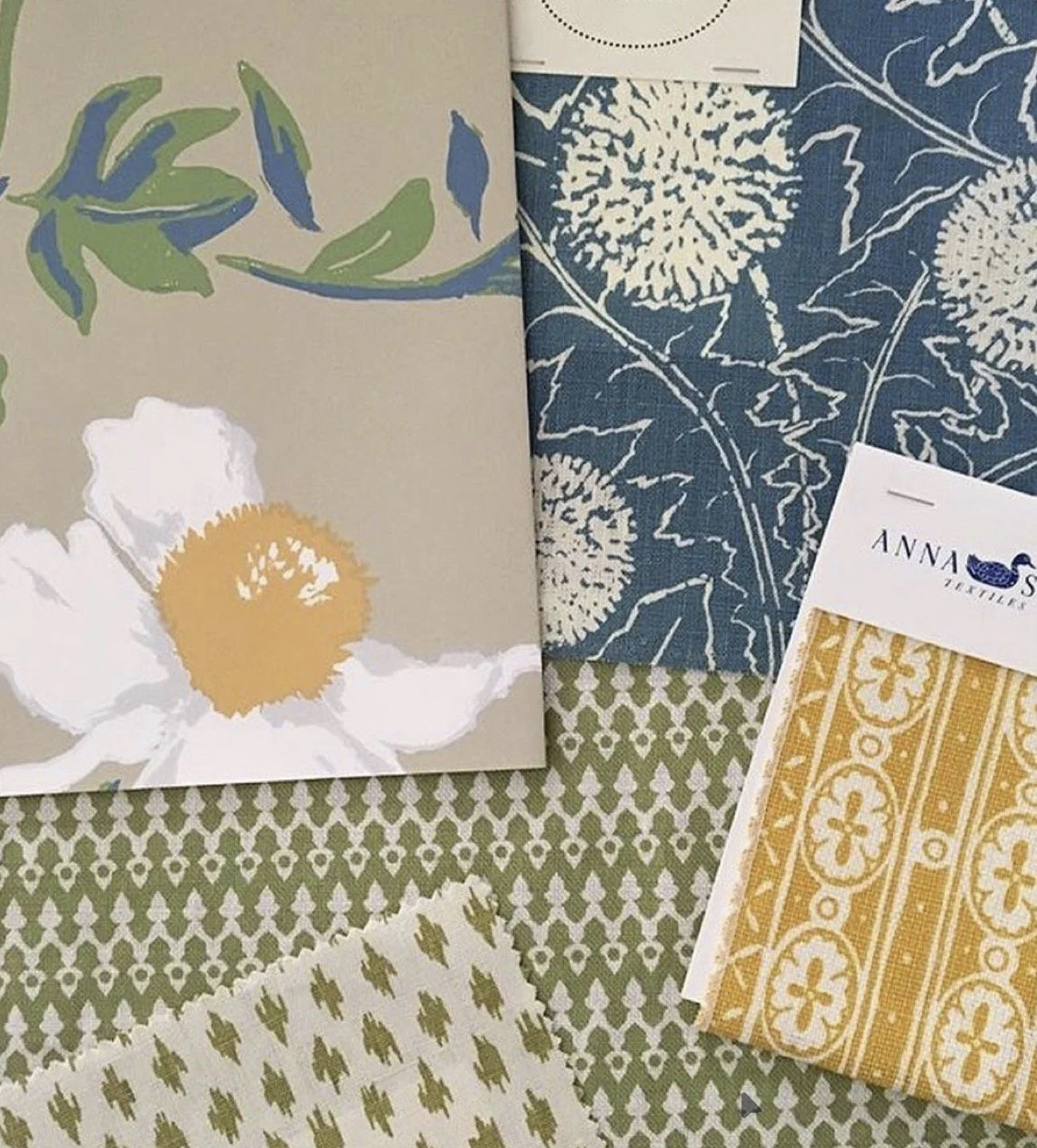 A display of various patterned cloth samples and a floral card with a white flower and yellow center.