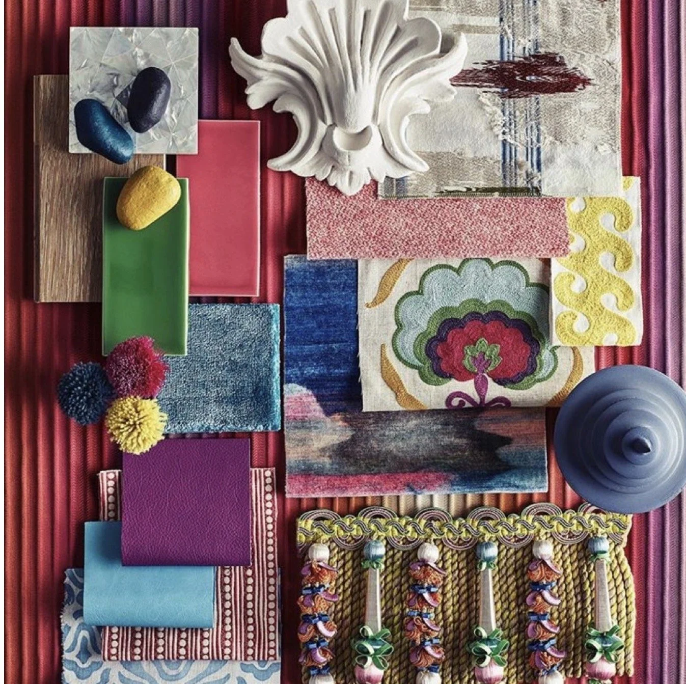 A collection of interior design and decor items, including fabric samples, textured tiles, decorative objects, and a white ornamental wall piece, arranged on a pink background.