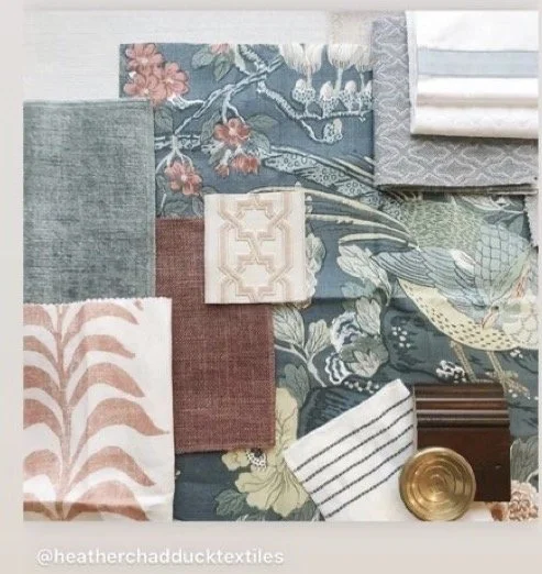A collection of fabric swatches in various colors and patterns, including floral, striped, and solid designs, along with a small brass bowl, a wooden piece, and a white chipboard with embossed design.