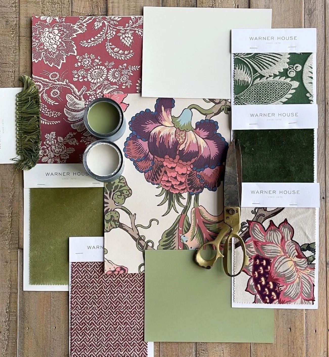 Interior design fabric and paint samples, including floral and geometric patterns, green and pink color swatches, gotten from Warner House, along with painter's scissors, small candles, and fabric samples on a wooden surface.