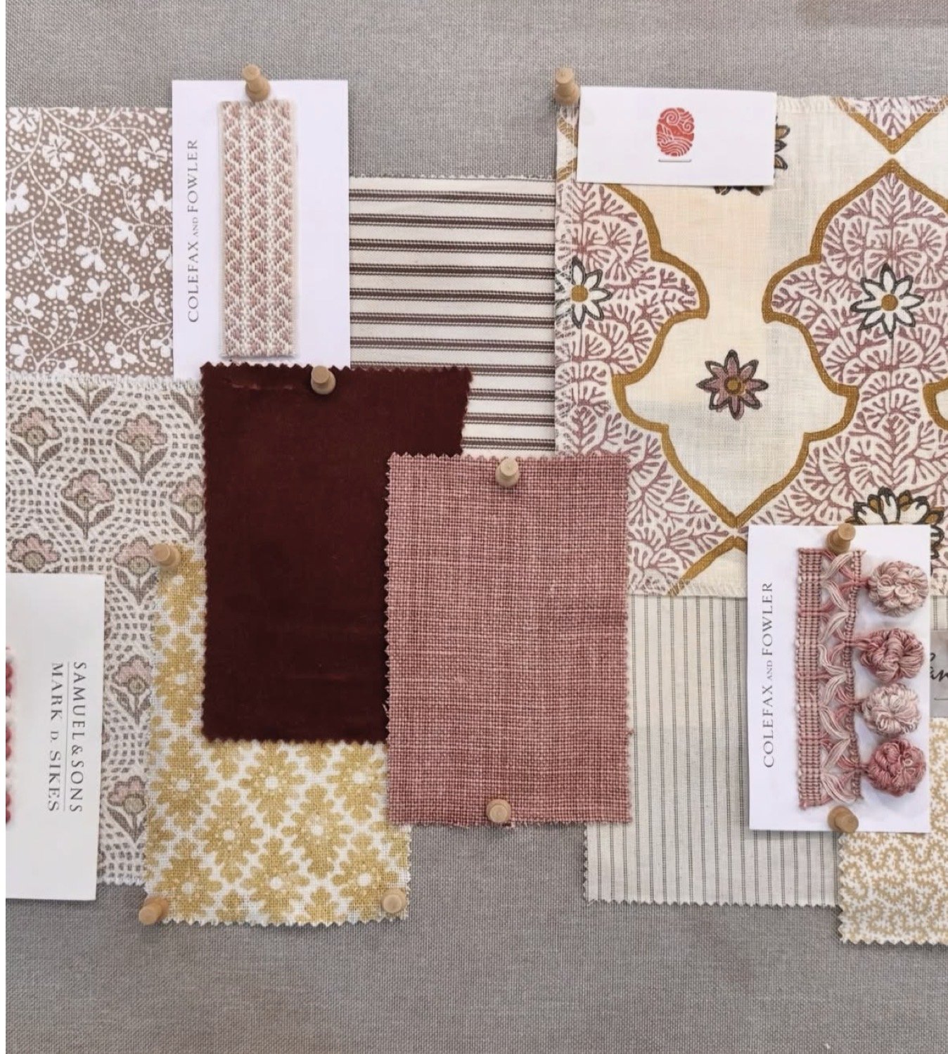 A fabric sample board with various textile swatches in pink, beige, and burgundy tones, pinned on a gray background. The fabrics display different patterns including floral, geometric, and striped designs.