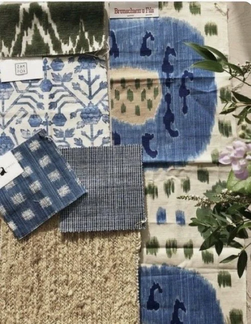 Arrangement of various fabric swatches with blue and white patterns, a small green plant, and a section of beige textured carpet.