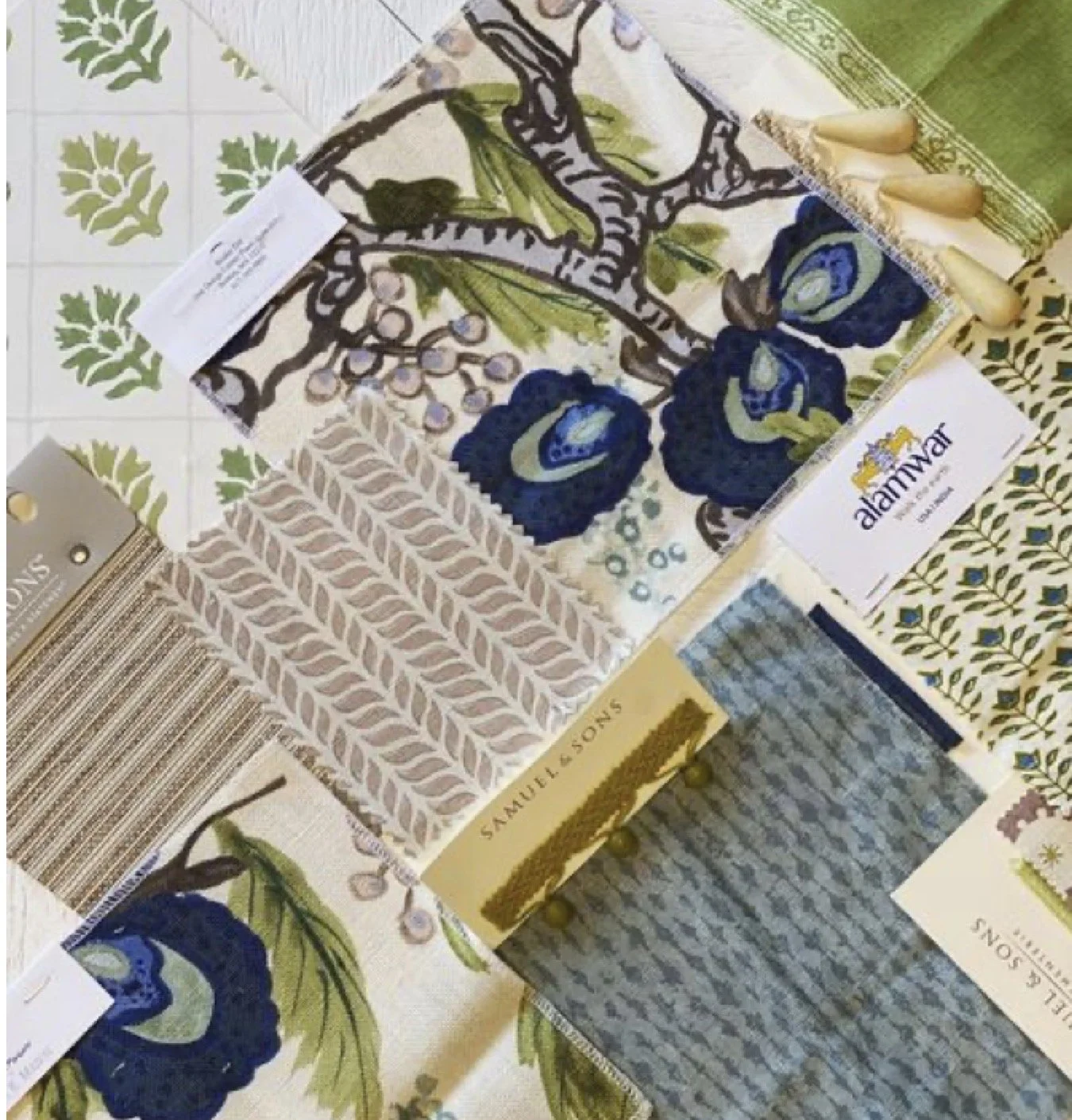 Display of fabric sample swatches with floral and abstract patterns in shades of blue, green, beige, and white, along with sample cards and tags from samuele sons and alaminar.