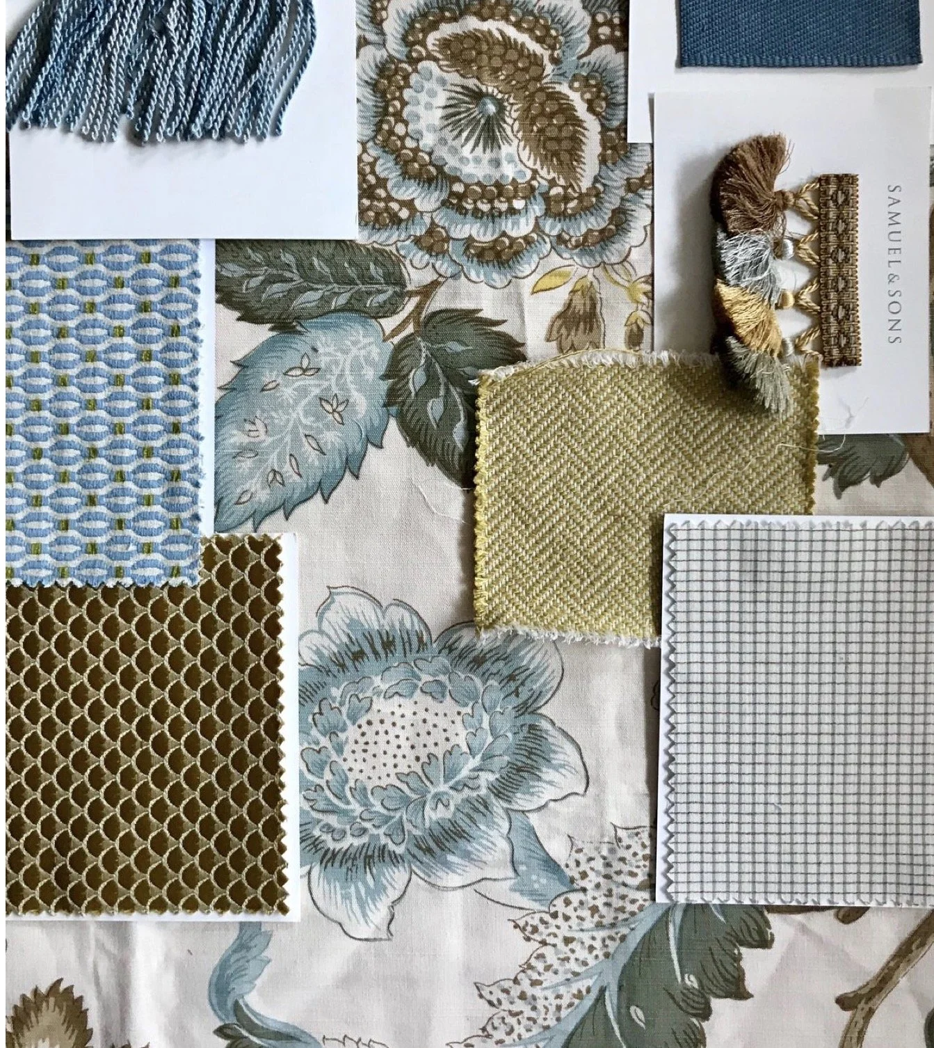 A collection of fabric swatches, tassels, and textile pattern samples laid out on a floral-printed cloth.