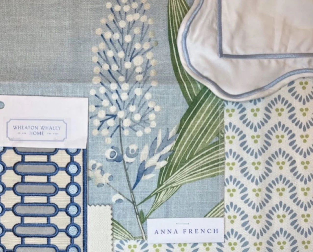 Fabric samples with botanical and geometric patterns, along with a linen napkin, labeled 'Wheaton Whaley,' 'Anna French,' and a fabric with blue and white designs.