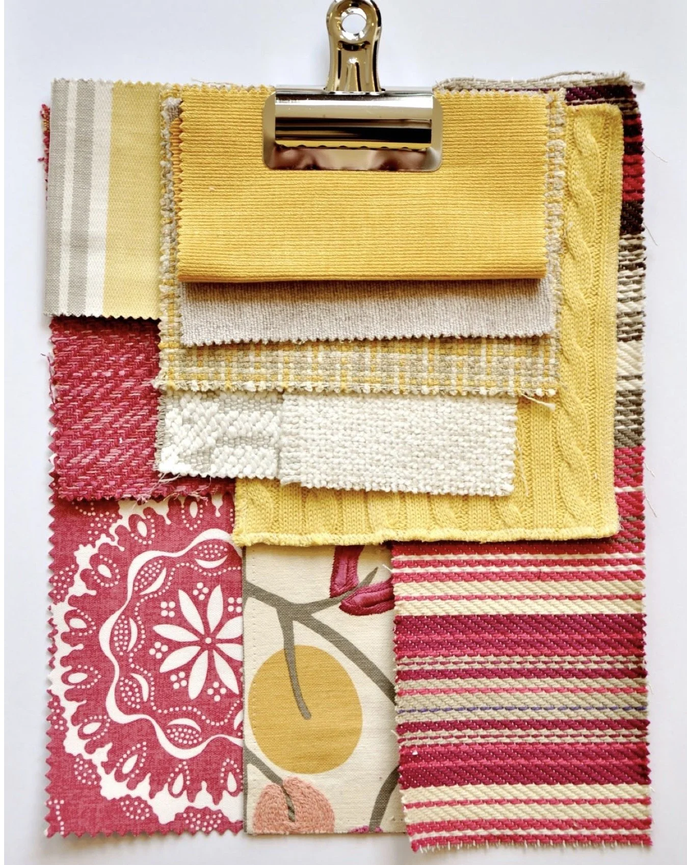 A color swatch sample card with various fabric and textile samples in yellow, pink, cream, and patterned designs, attached to a metal clip at the top.