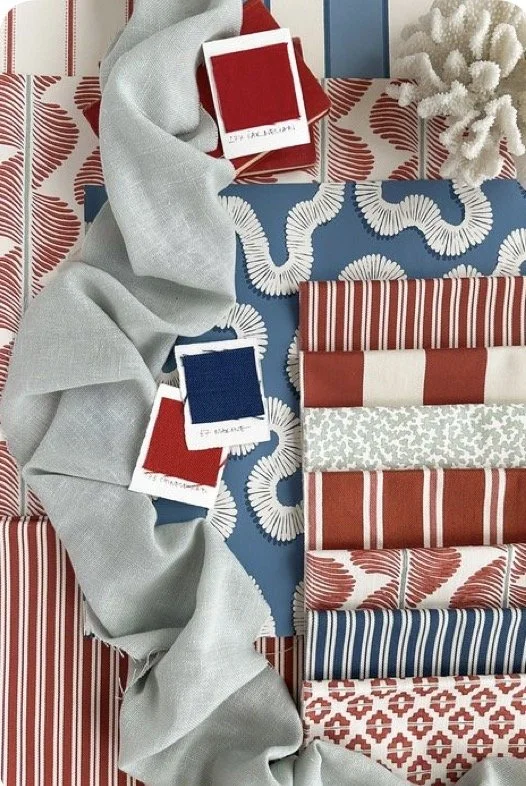 Collection of fabric swatches in red, white, blue, and gray, with two color sample cards and a twisted gray fabric, arranged with patterned and striped textiles.