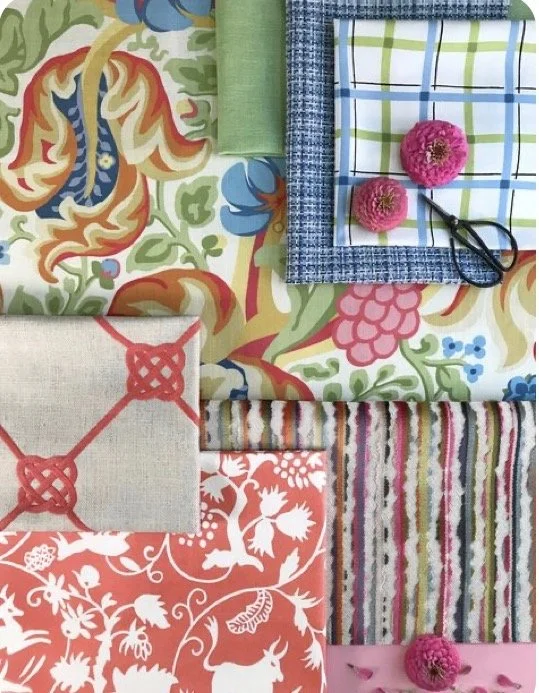 A vibrant assortment of fabric swatches and textiles with various patterns and colors, including floral, plaid, striped, and solid, some decorated with pink flowers and scissors.